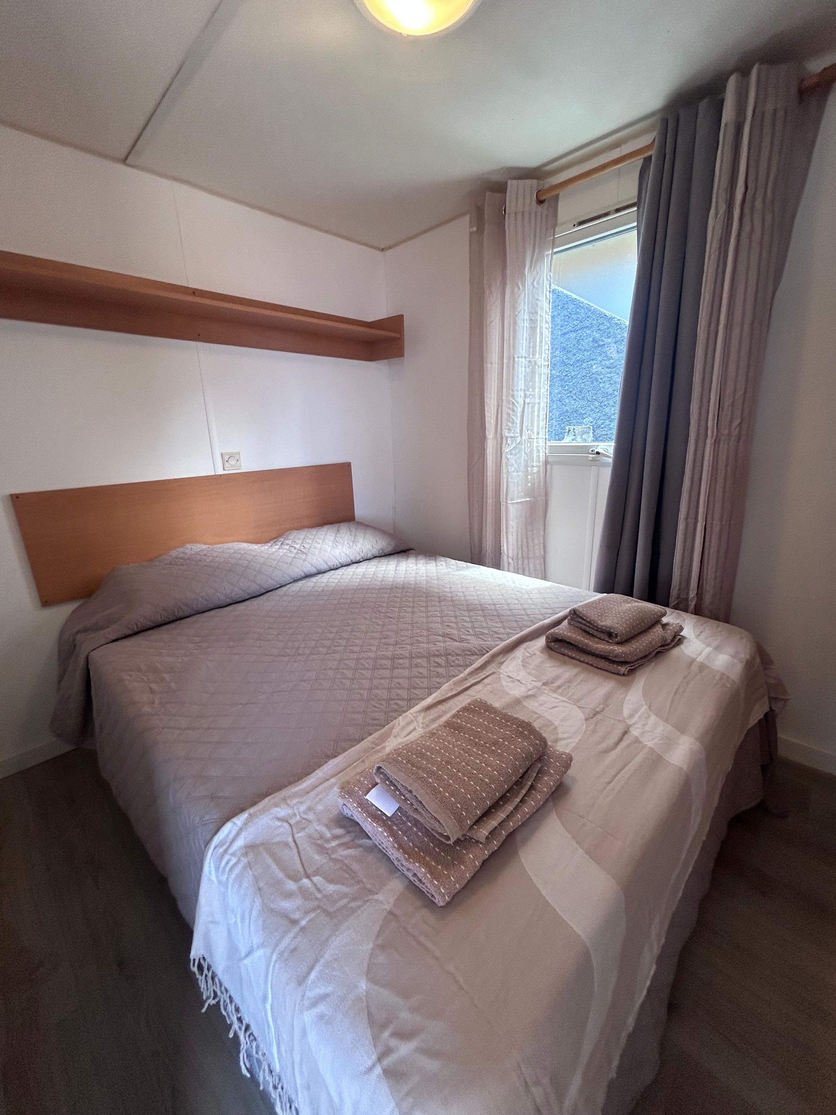 Ein Schlafzimmer mit einem großen Bett, einem Holzkopfstück, einem Fenster mit Vorhängen und Blick auf einen Berg.