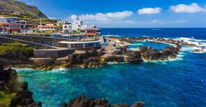 A coastal hotel with a pool, rocky shoreline, and clear blue sea.