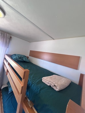 A single bed with a wooden headboard, a green bedspread, and a beige blanket.