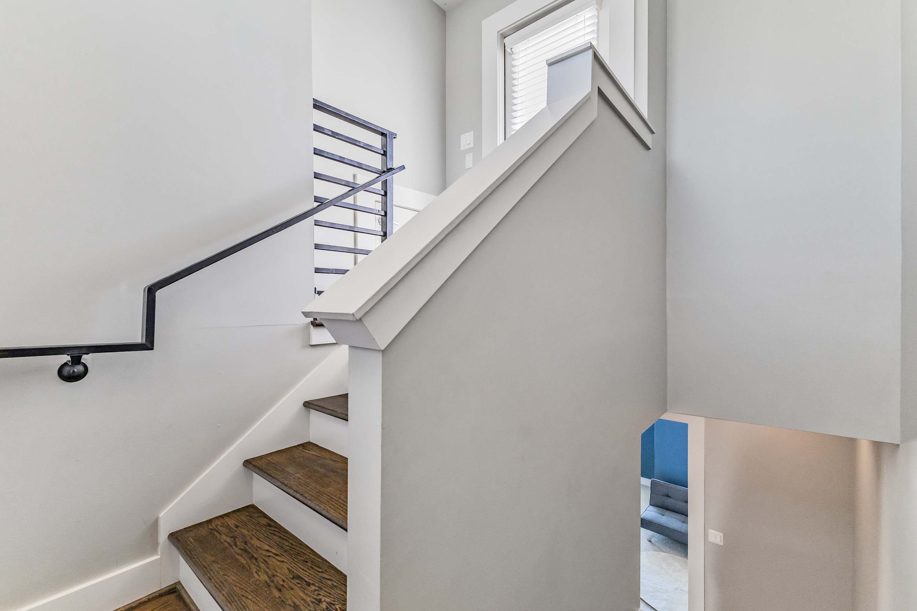 A staircase with wooden steps and a metal handrail, leading to a landing with a window.
