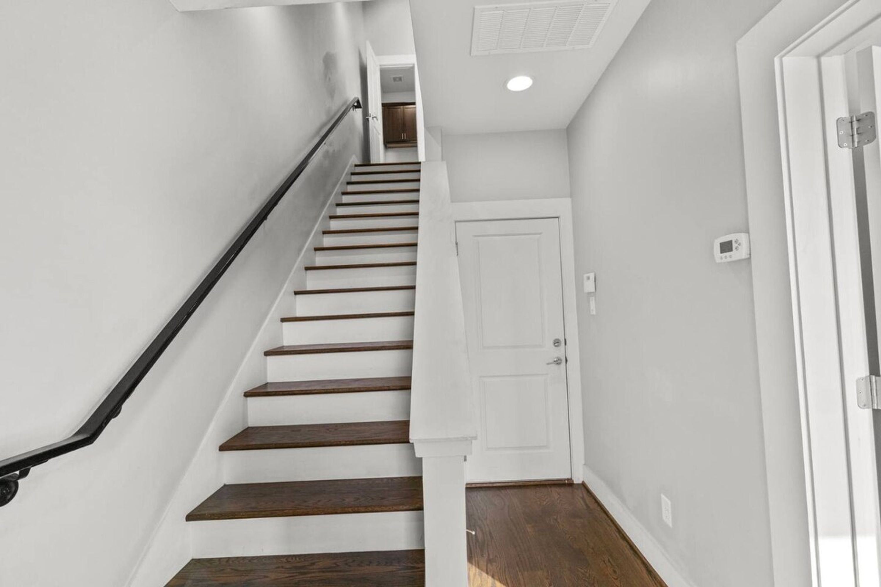 Una escalera con peldaños de madera y barandilla negra que conduce a una puerta blanca.