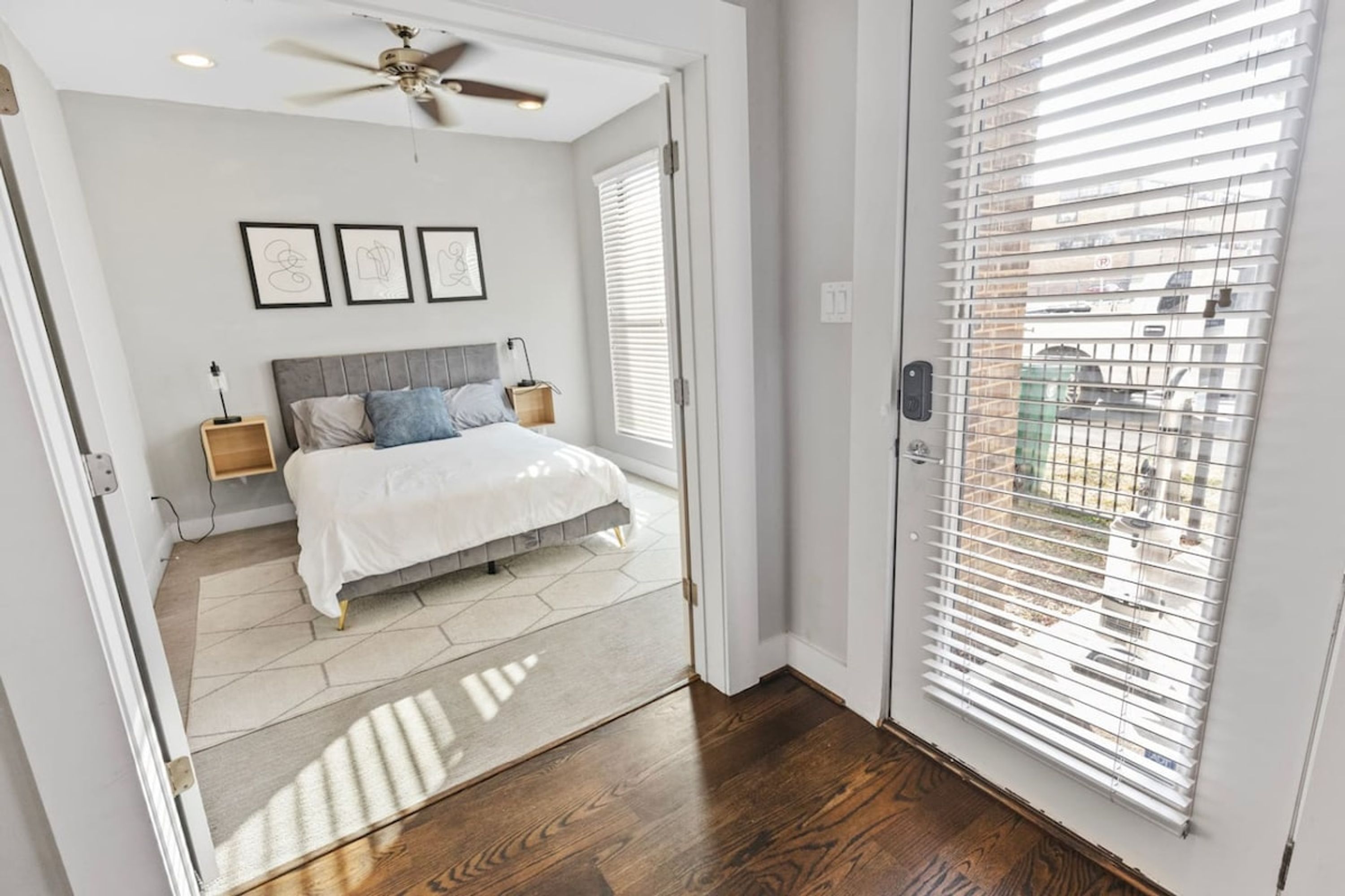 A bedroom with a bed, nightstands, a ceiling fan, and a view through a window with blinds.