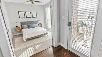 A bedroom with a bed, nightstands, a ceiling fan, and a view through a window with blinds.