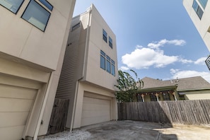 A residential building with a garage, a wooden fence, and a clear sky. - Houston Townhome w Skyline Views Rooftop Patio (Houston)