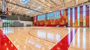 A basketball court with a wooden floor and red lines, large windows, and a high ceiling with visible ductwork.