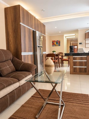 A modern living room with a sofa, a glass coffee table, and a kitchen area with a refrigerator and a coffee maker. - Walk to Telef Rico and Megacenter I 2BR I Parking (La Paz)