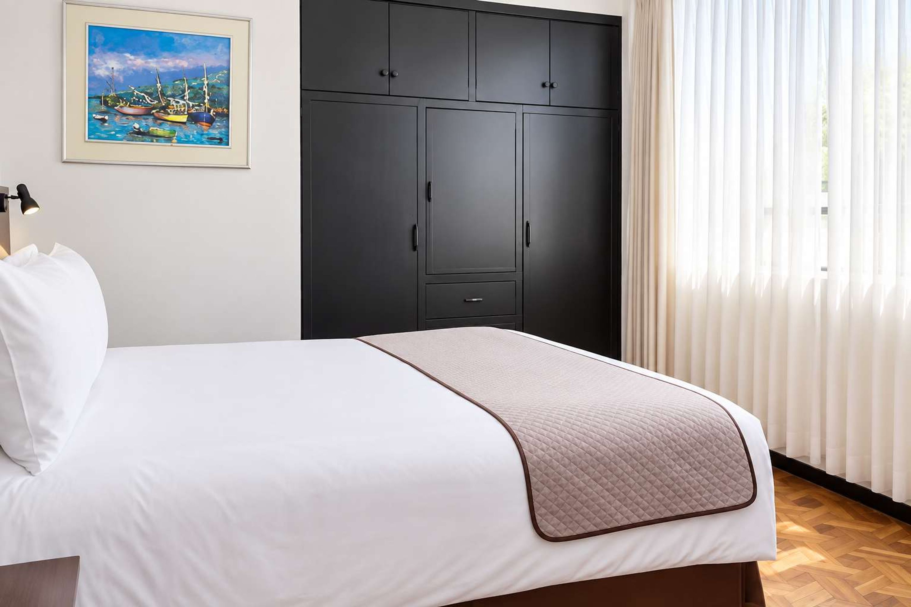 A hotel room with a bed, a wardrobe, and a painting on the wall.