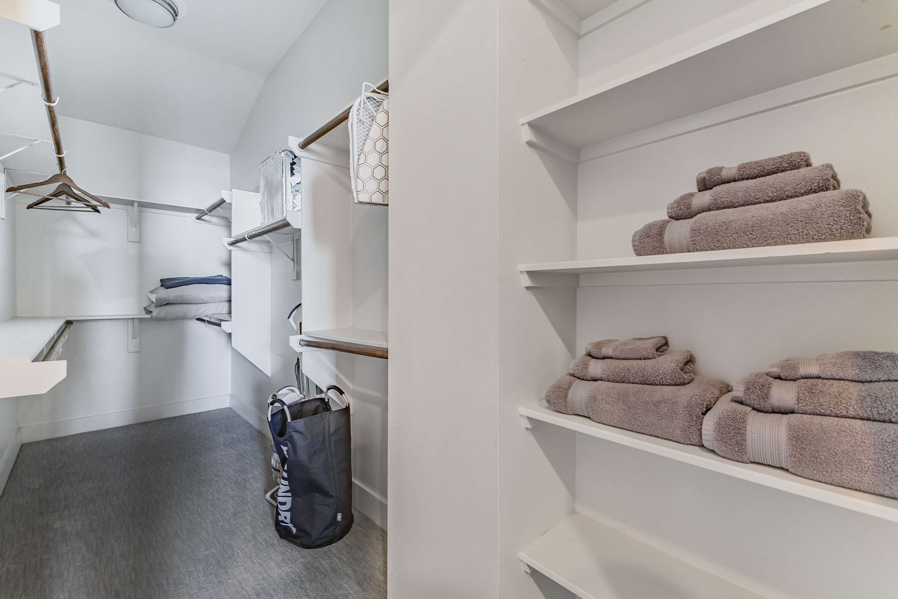 A hotel room with a grey carpet, a hanging laundry bag, a white towel, and a shelf with folded towels.
