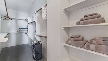A hotel room with a grey carpet, a hanging laundry bag, a white towel, and a shelf with folded towels.