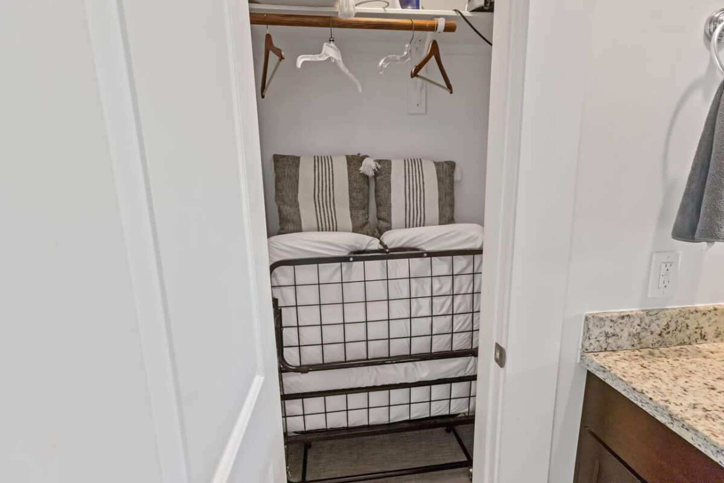 A compact room with a bed, a metal storage unit, and a small bathroom area with a sink and towel rack.