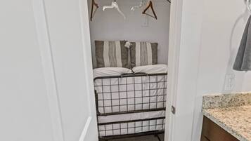 A compact room with a bed, a metal storage unit, and a small bathroom area with a sink and towel rack.
