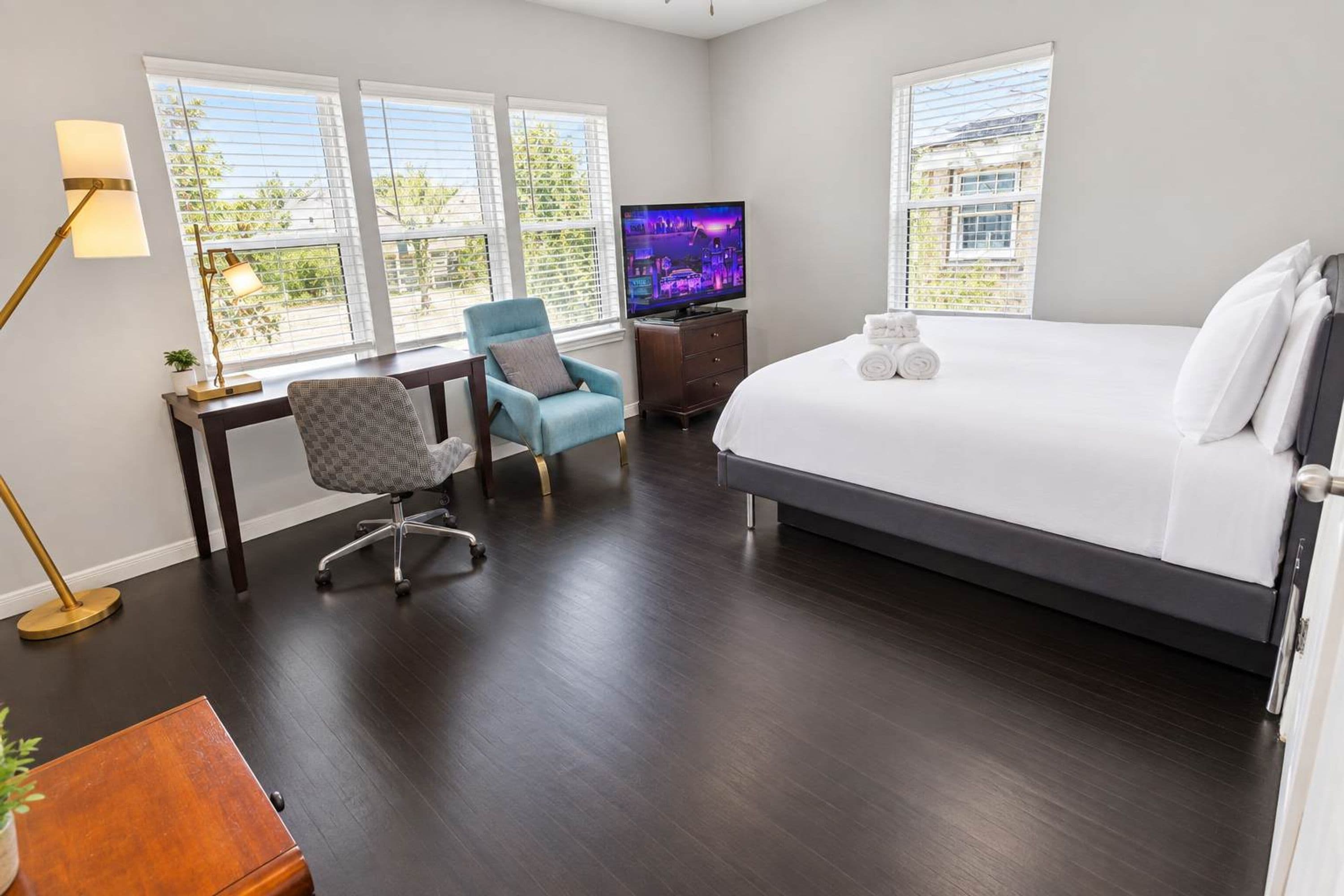 A hotel room with a large bed, a desk with a chair, a television, and a window with blinds.