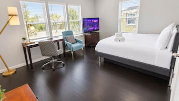 A hotel room with a large bed, a desk with a chair, a television, and a window with blinds.
