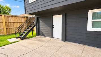 Un edificio residencial con fachada gris, una puerta blanca y una escalera negra que lleva a una terraza.