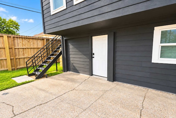 Edifício residencial com fachada cinza, porta branca e escada preta que dá para um deck.