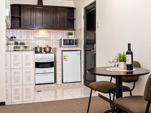 A compact kitchen with a stove, oven, microwave, and refrigerator. There is a dining table with chairs and a wine bottle. - Calacoto Apt Kitchenette Zona Sur Sleeps 2 (La Paz)