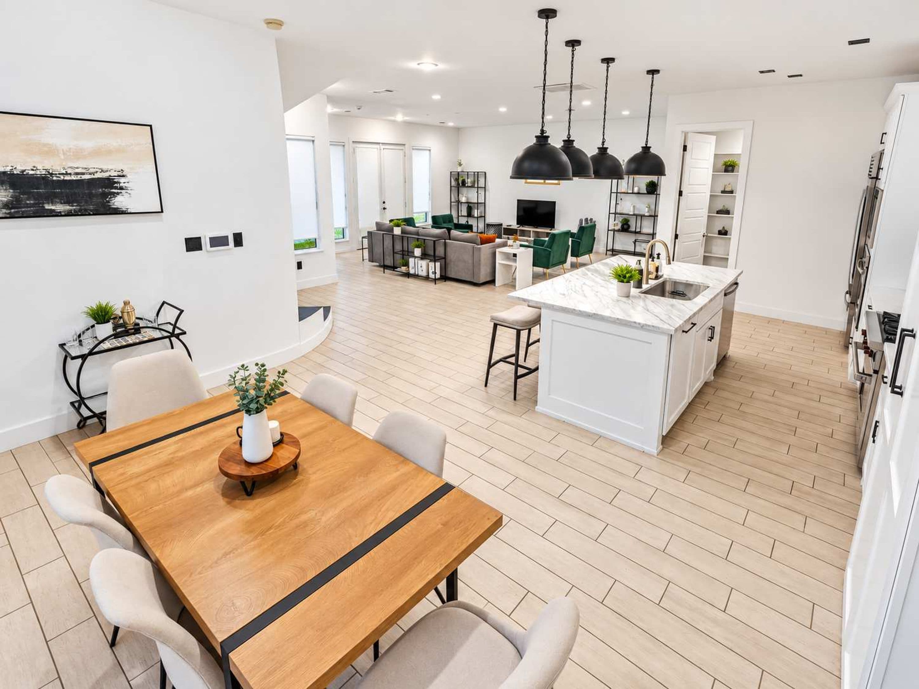 Cocina moderna con isla central, iluminación colgante y comedor con mesa y sillas de madera.