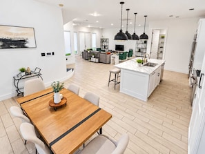 Cocina moderna con isla central, iluminación colgante y comedor con mesa y sillas de madera.