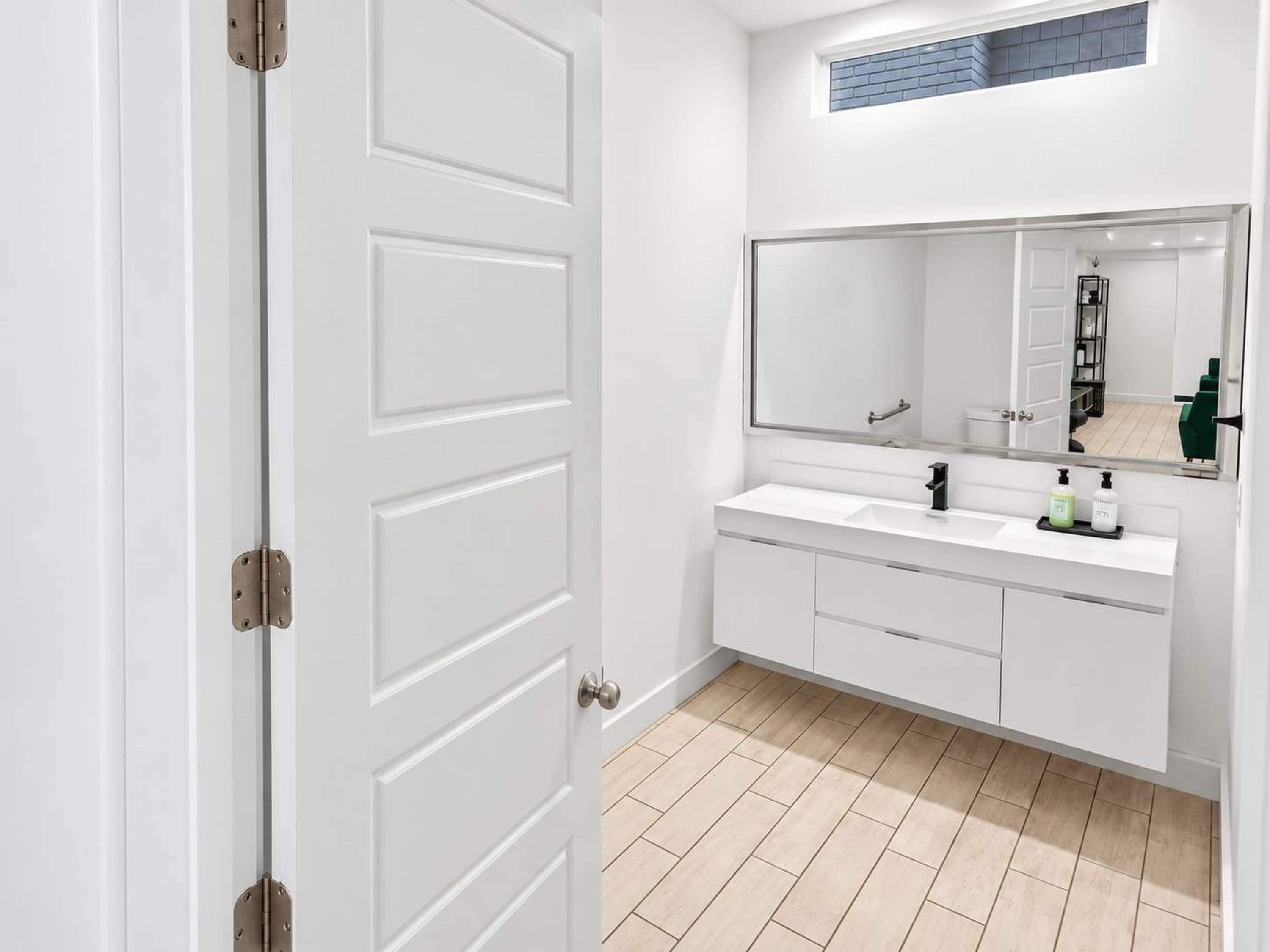 A modern bathroom with a white vanity, a large mirror, and a door with a handle.