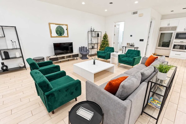 A modern living room with green sofas, a grey sofa, a coffee table, and a TV. - Montrose Rooftop Townhome 3 Suites Sleeps 8 (Houston)