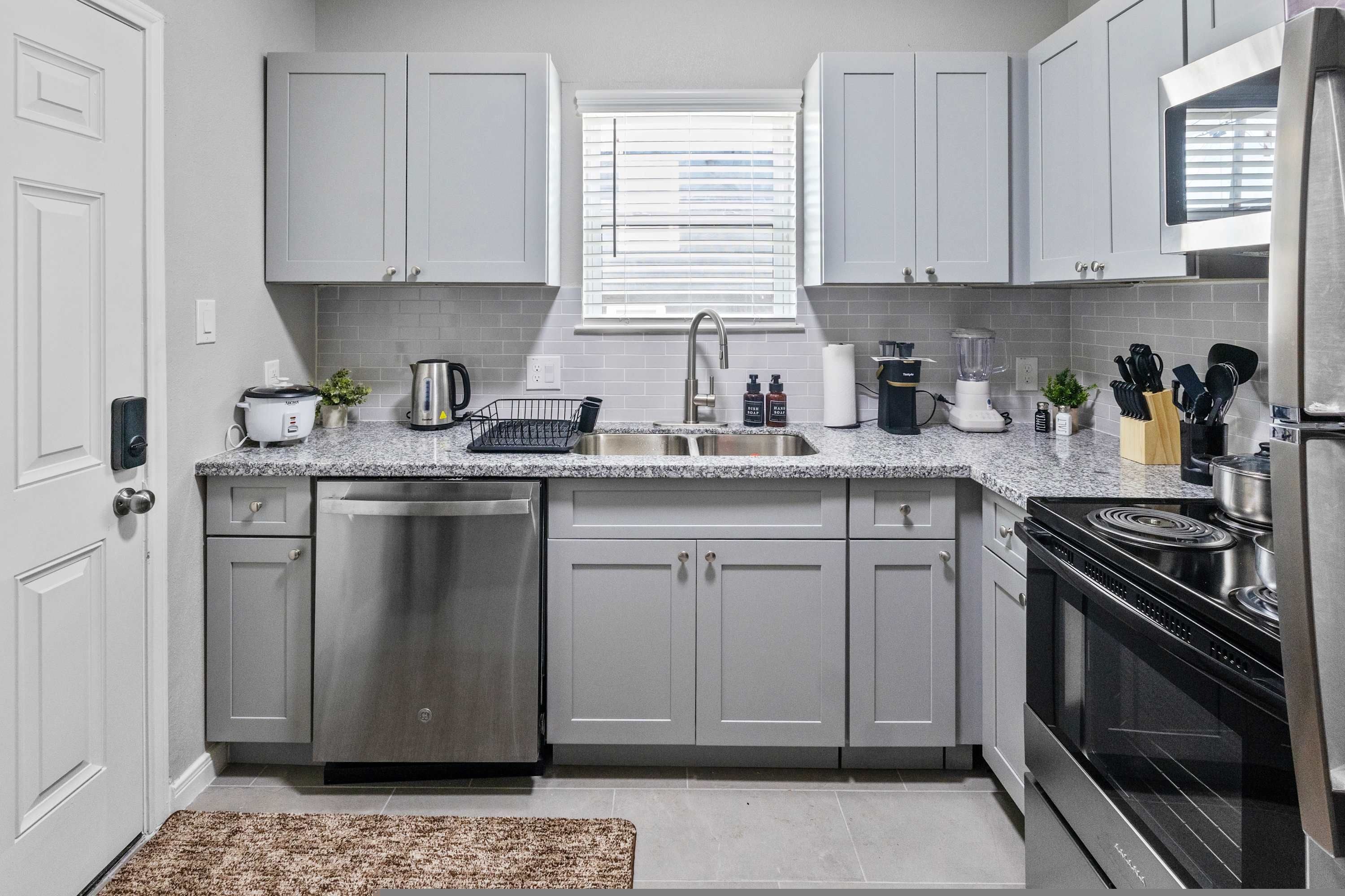 A modern kitchen with grey cabinets, a stainless steel dishwasher, a built-in oven, and a granite countertop.