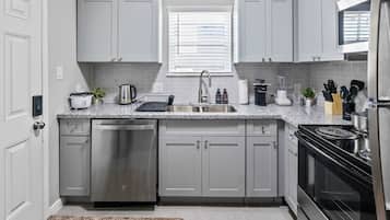 A modern kitchen with grey cabinets, a stainless steel dishwasher, a built-in oven, and a granite countertop.