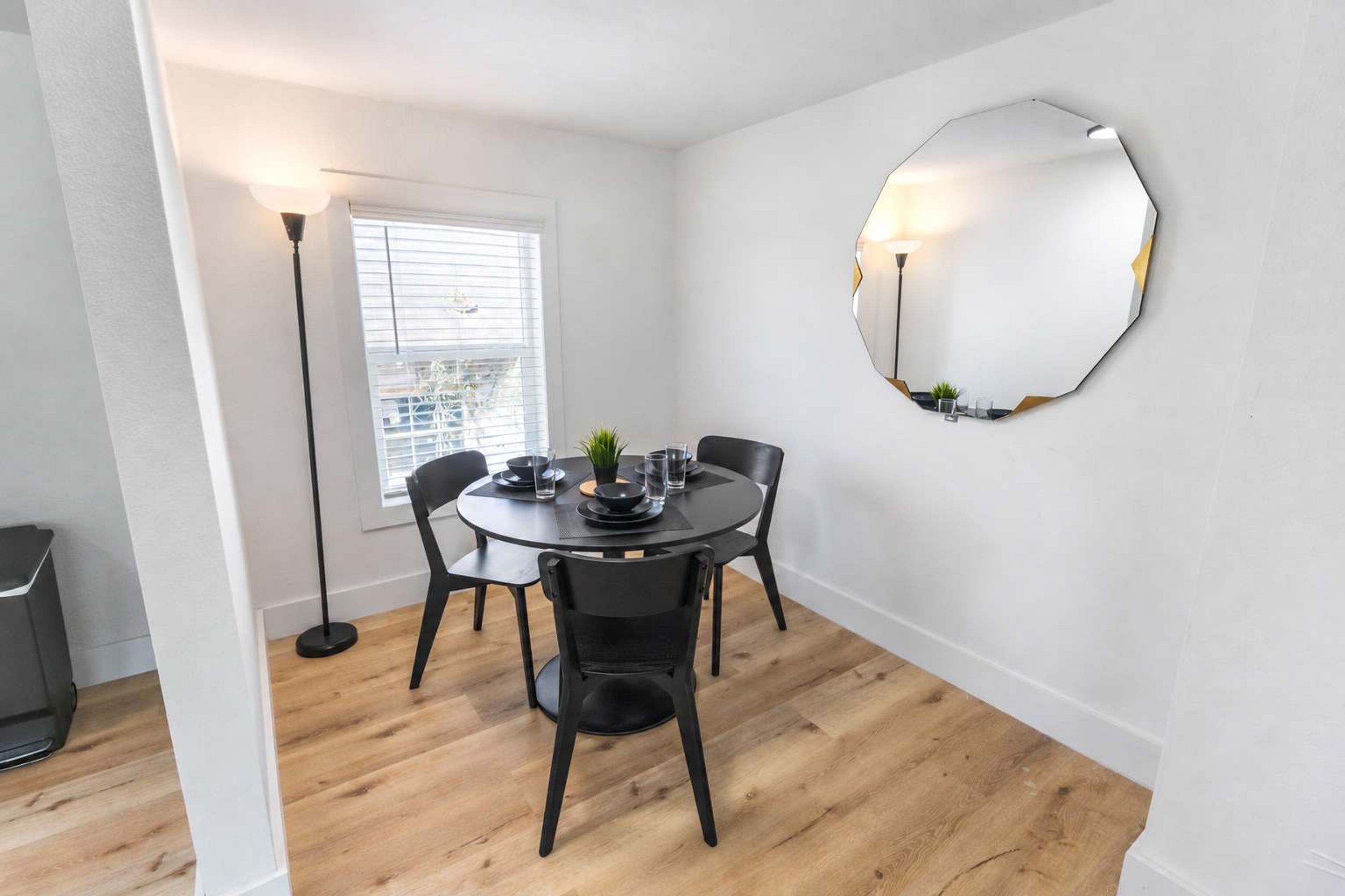 A dining area with a round table, black chairs, a floor lamp, and a wall-mounted mirror.