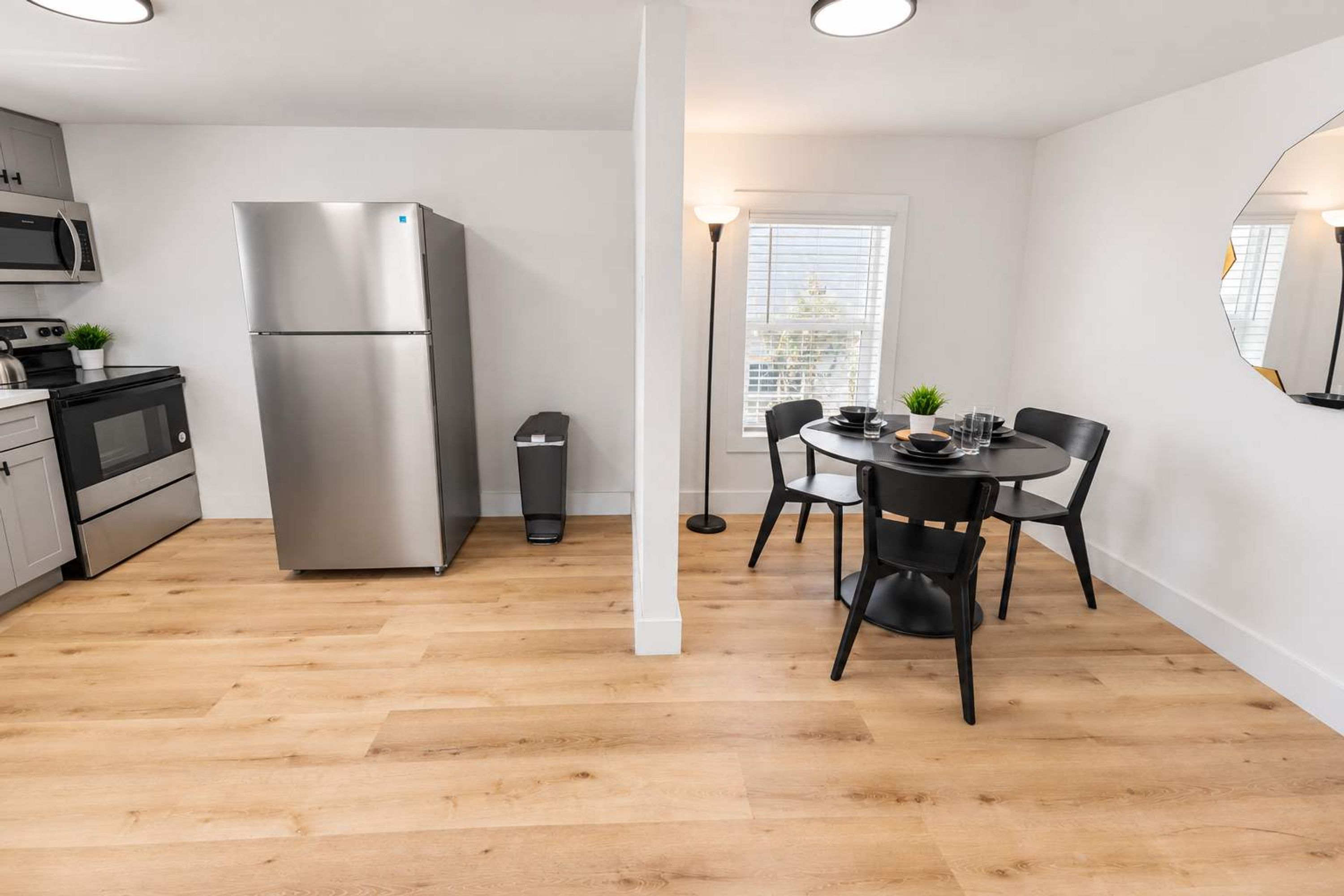 A modern kitchen with a stainless steel refrigerator, a microwave, and a stove. There is a dining area with a round table and chairs.