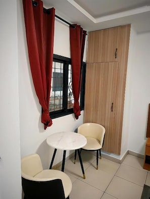 Una habitación pequeña con ventana, dos sillas, una mesa redonda y un armario de madera.