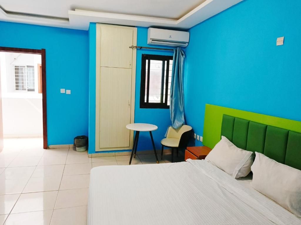 A hotel room with a bed, a small table, a chair, a window with curtains, and an air conditioning unit.