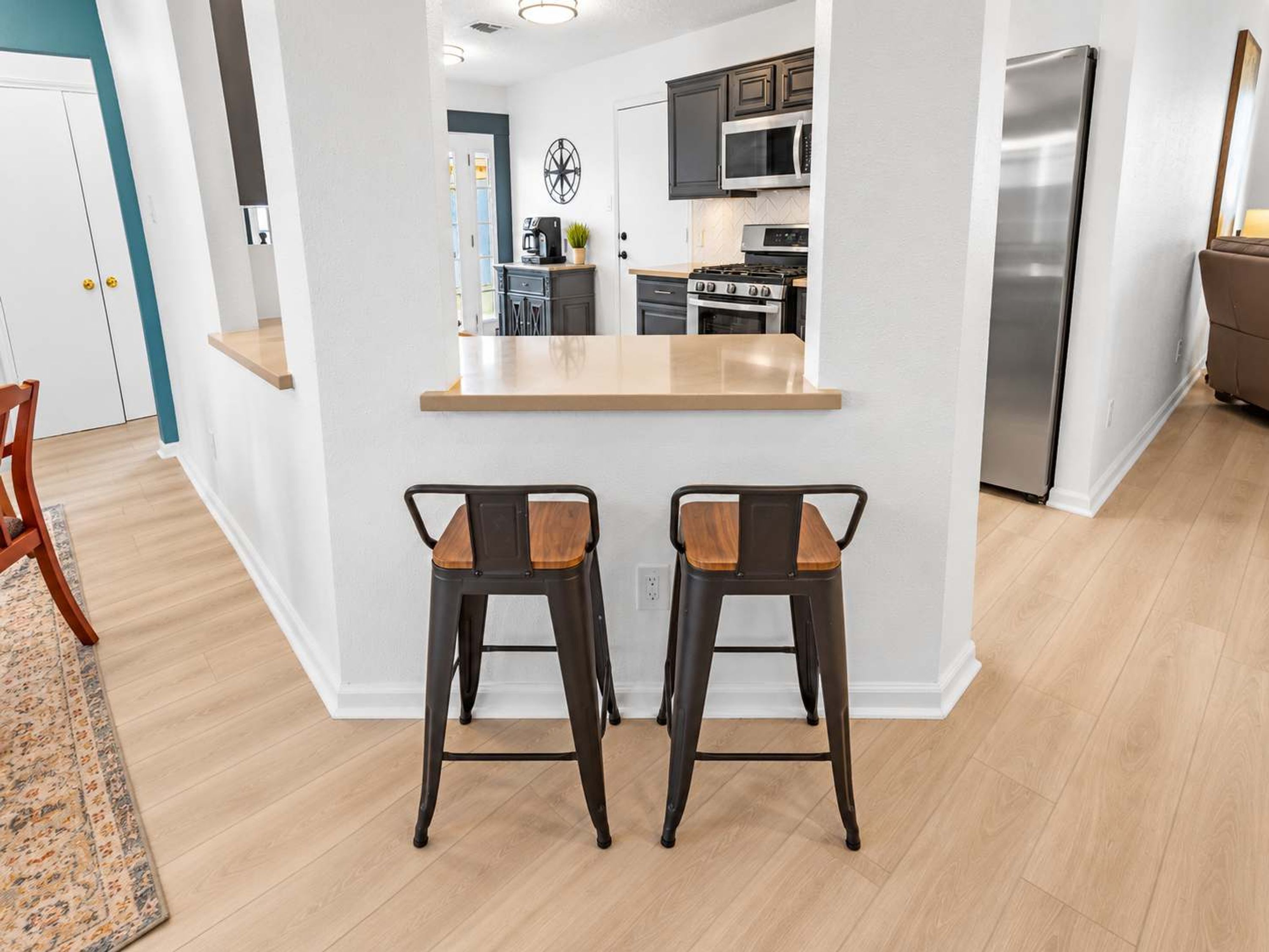 A modern kitchen with a central island, two bar stools, and a stainless steel refrigerator.