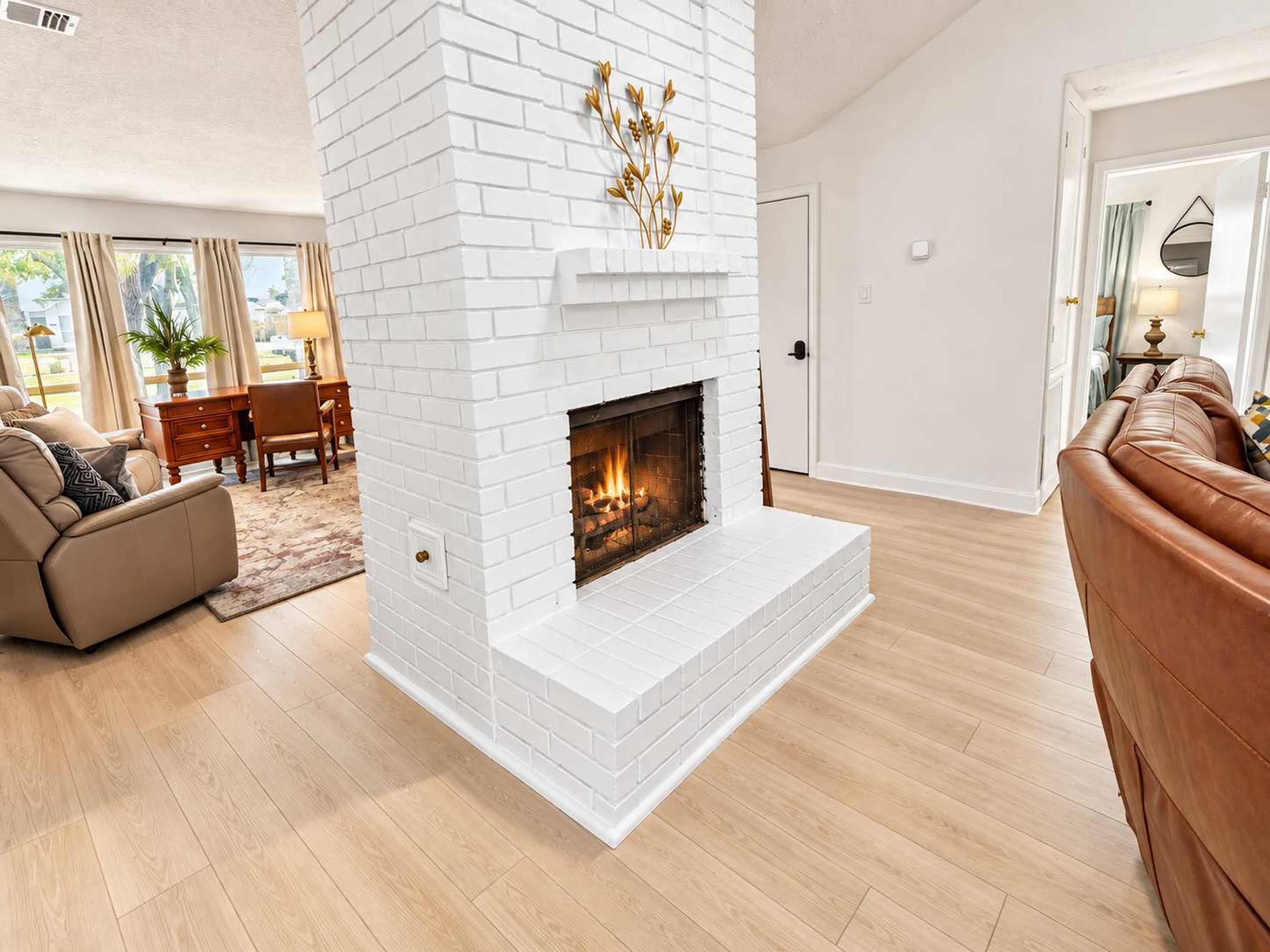 A living room with a white brick fireplace, a leather sofa, and a wooden floor.