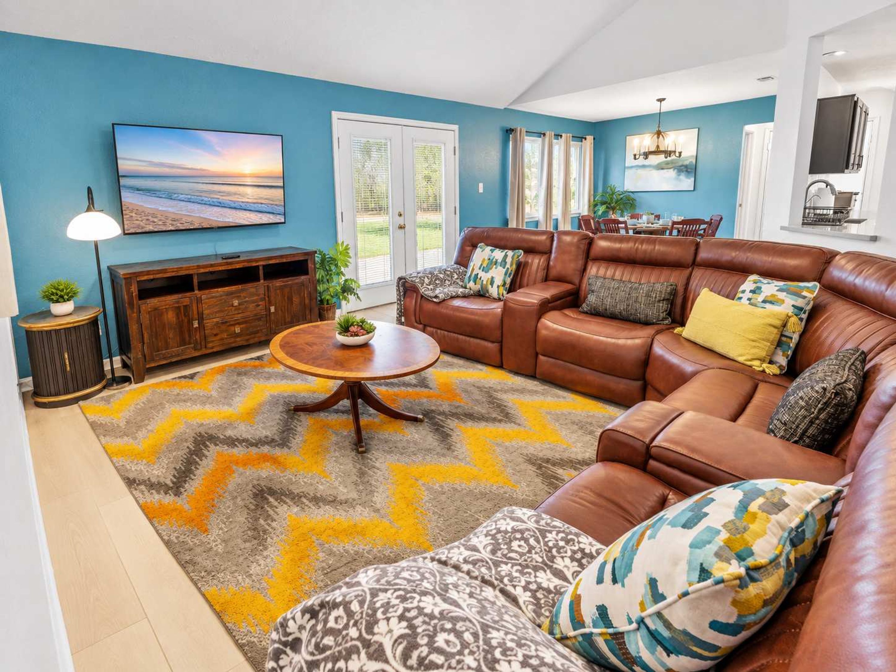 A living room with a brown leather sofa, a round coffee table, and a blue wall with a painting.