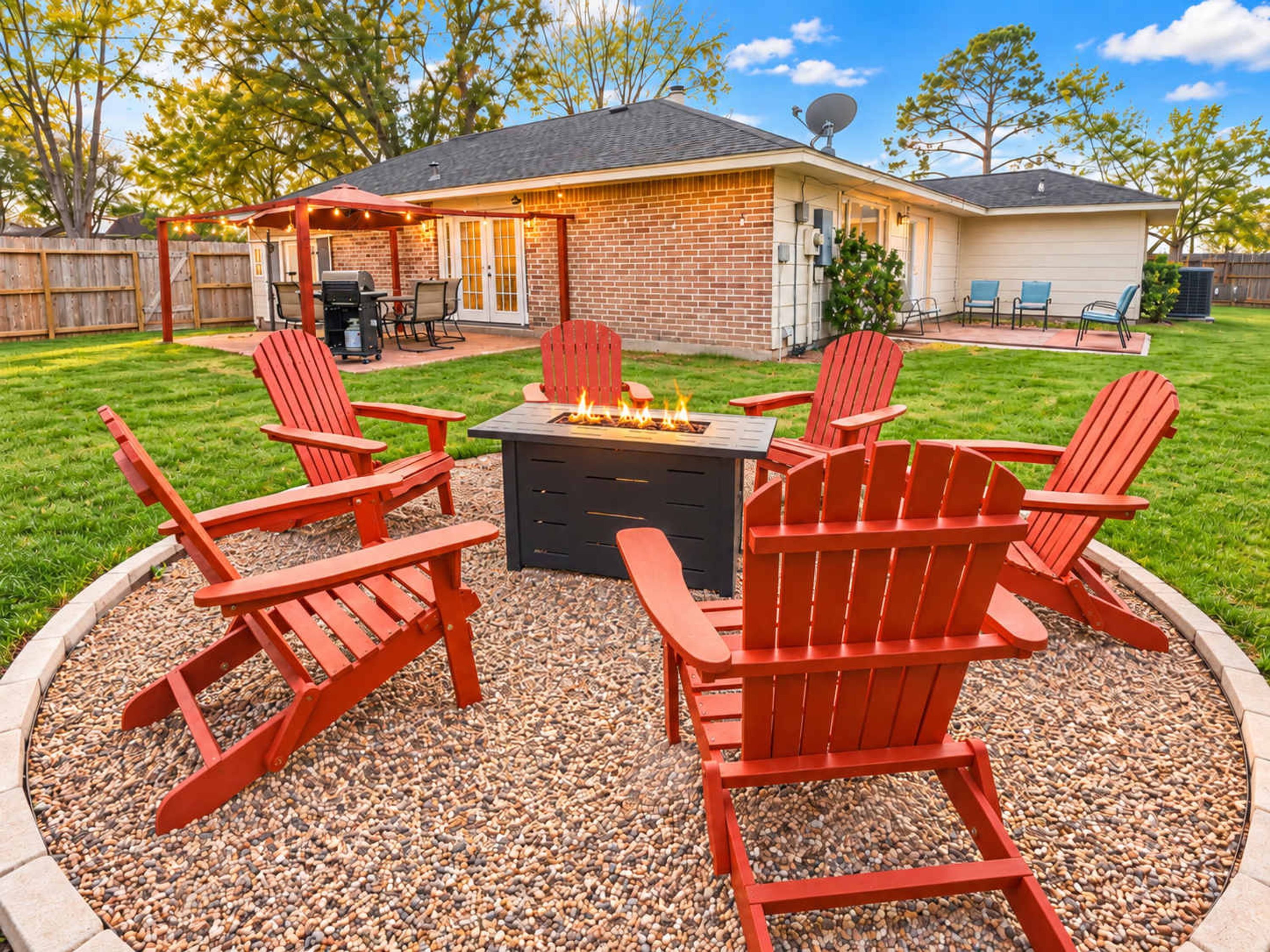 A backyard with a fire pit, red Adirondack chairs, and a brick patio.