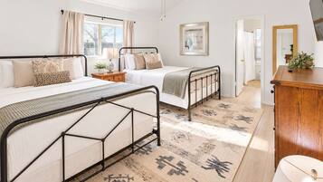 Quarto com duas camas, cômoda de madeira, espelho e janela com cortinas.