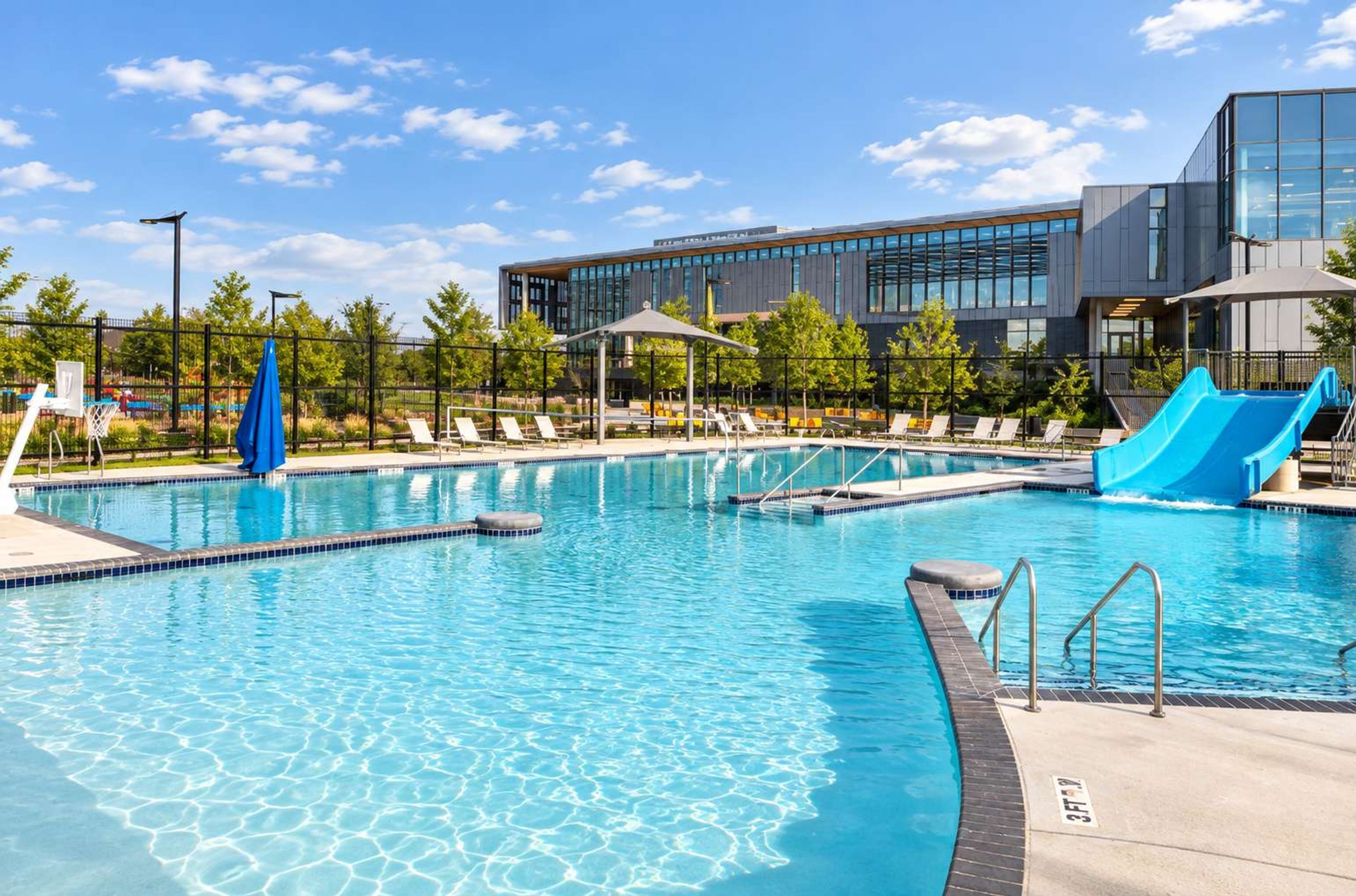 A swimming pool with a slide, lounge chairs, and a modern building in the background.
