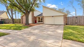 A residential house with a garage, a driveway, and a tree in the front yard.