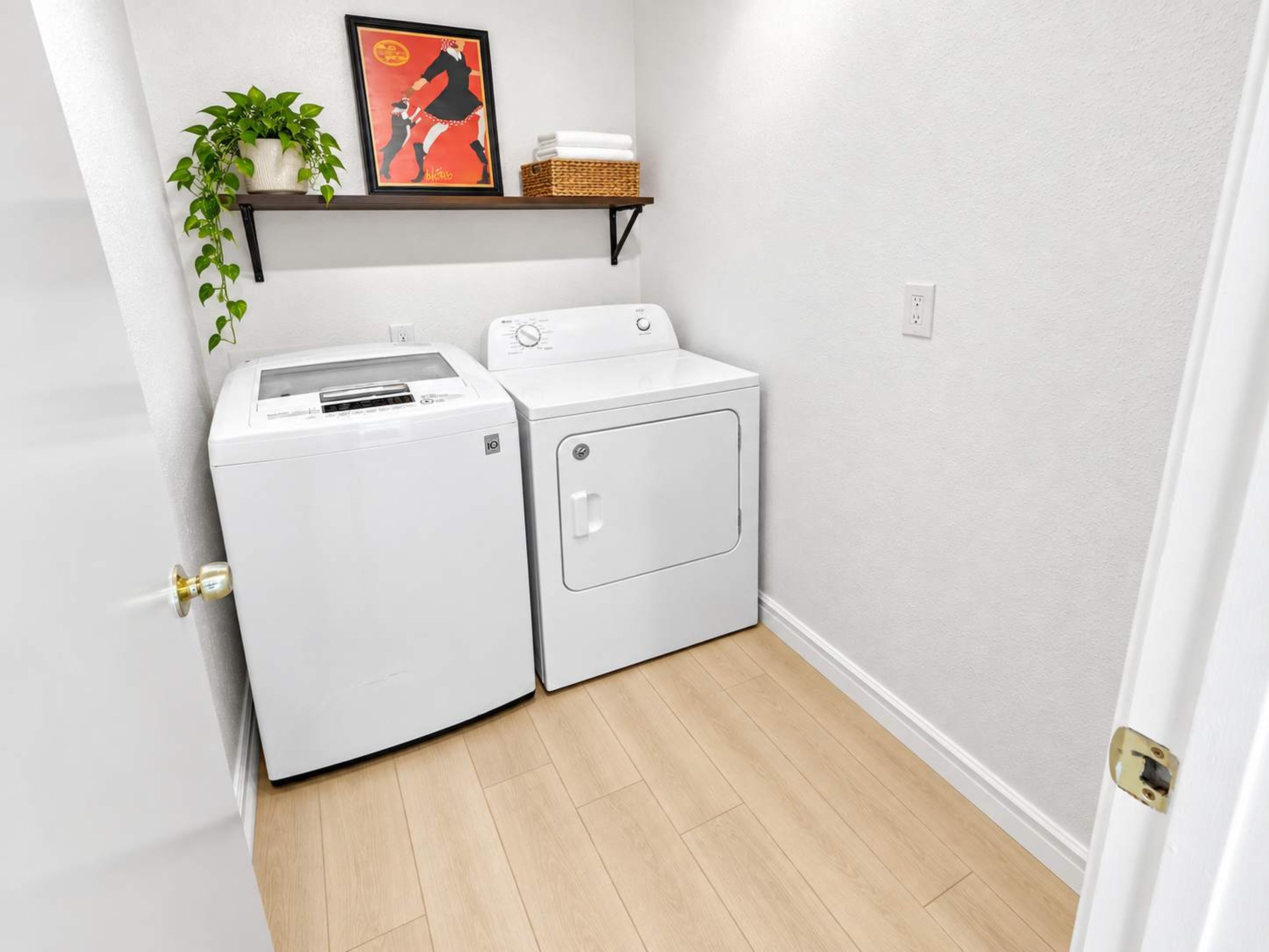 A laundry room with a washing machine, dryer, and a shelf with a plant and a basket.