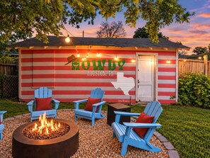Zona d'estar a l'aire lliure acollidora amb cadires Adirondack i una xemeneia, amb un edifici de fons que presenta un mapa de Texas i la indicació 'Howdy Houston, TX'.