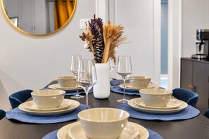 A dining table set with white bowls and wine glasses, a vase with dried flowers, and a blue placemat. - Honky Tonk Heights Home I 2 Kings I EV I Fire Pit (Houston)