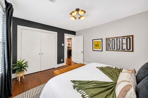A bedroom with a large bed, a ceiling light fixture, and two framed pictures on the wall. - Honky Tonk Heights Home I 2 Kings I EV I Fire Pit (Houston)