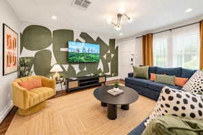 A modern living room with a sofa, armchair, coffee table, and a flat-screen TV mounted on the wall. - Honky Tonk Heights Home I 2 Kings I EV I Fire Pit (Houston)