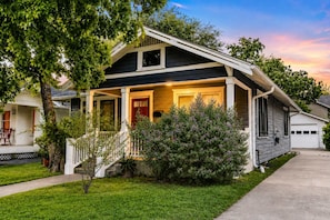 A two-story house with a front porch, a garage, and a well-maintained lawn. - Honky Tonk Heights Home I 2 Kings I EV I Fire Pit (Houston)