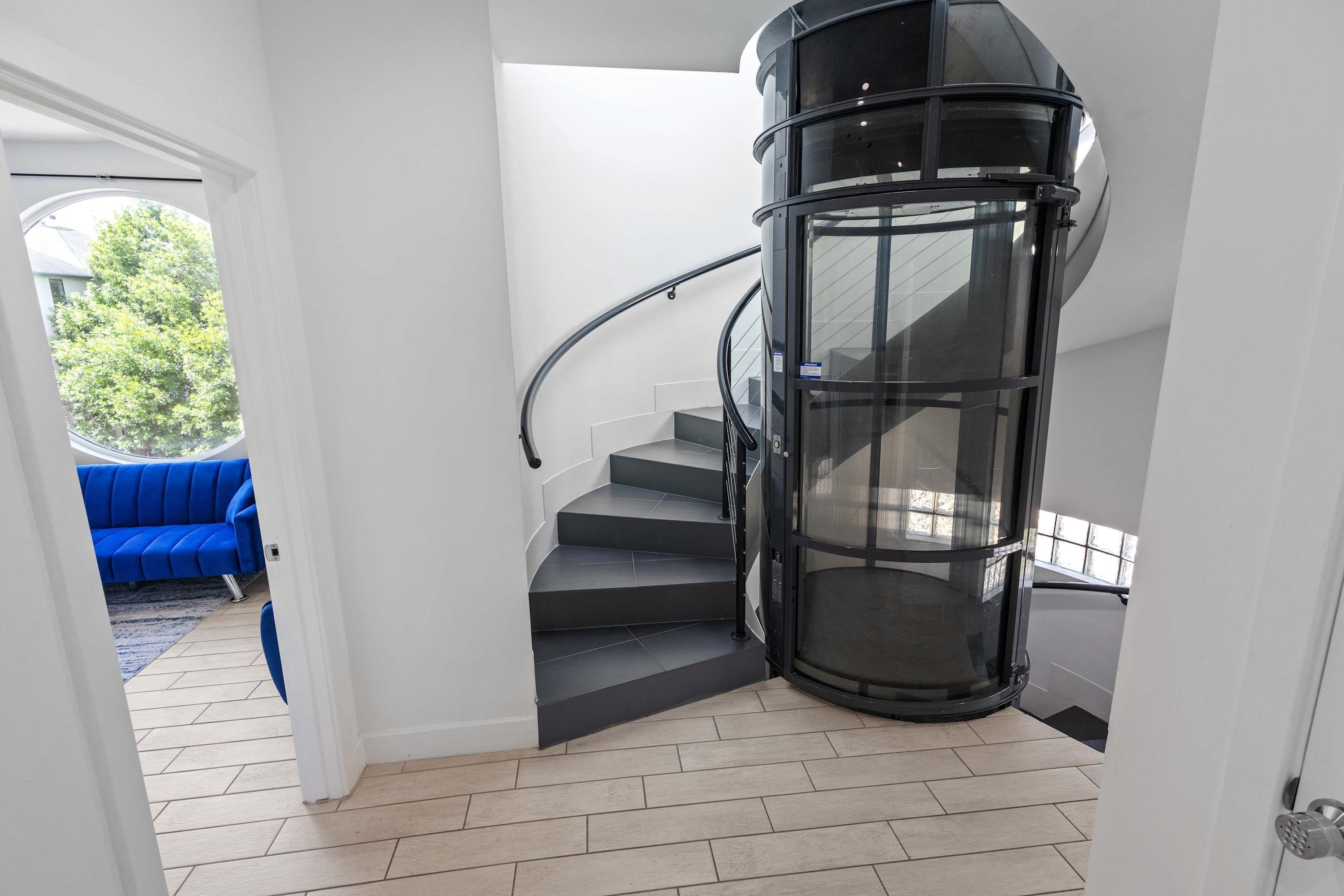 A modern interior with a spiral staircase, a blue sofa, and a view of greenery outside.