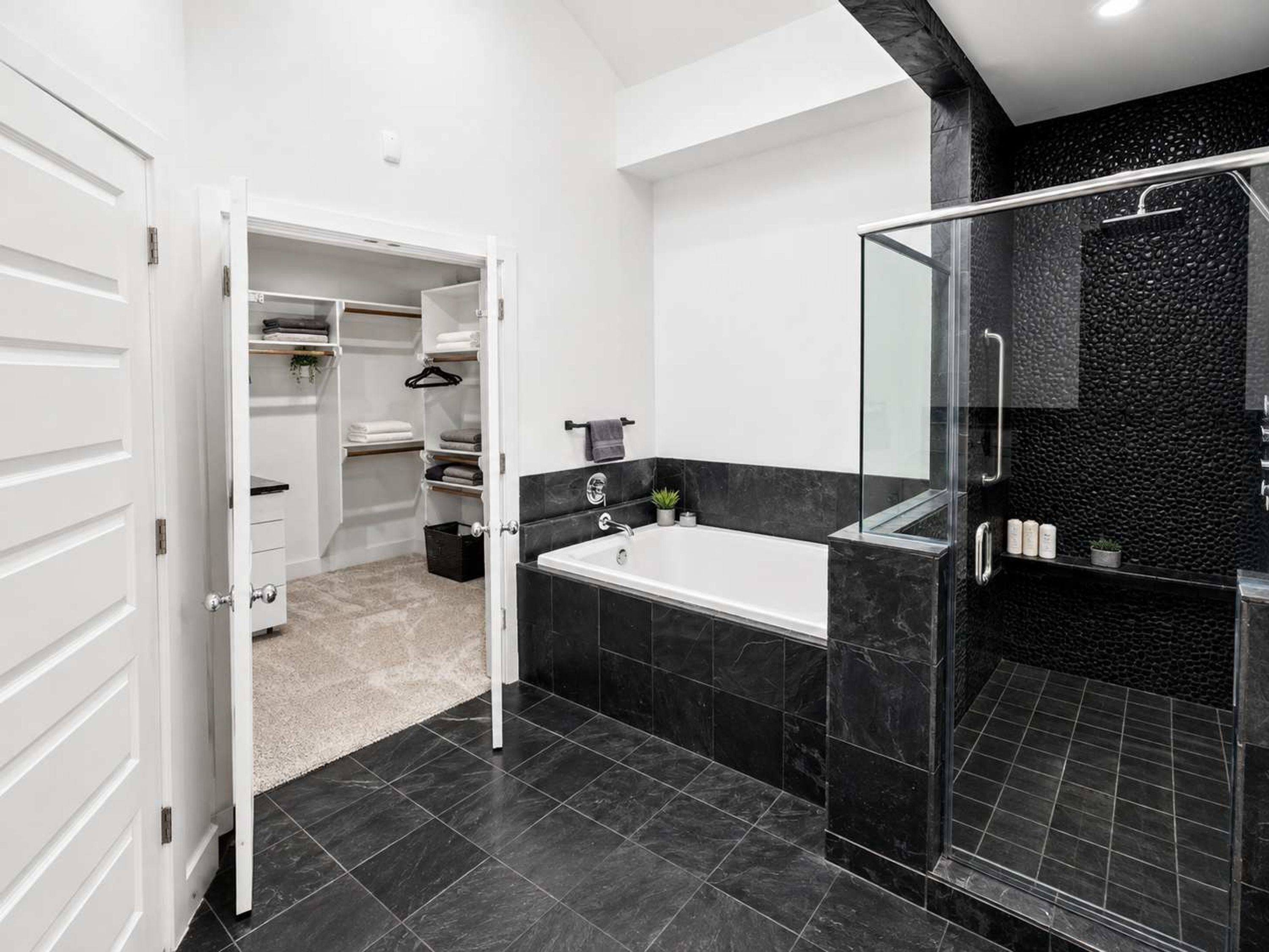 Un baño moderno con ducha envuelta en vidrio, una bañera blanca y un vestidor.