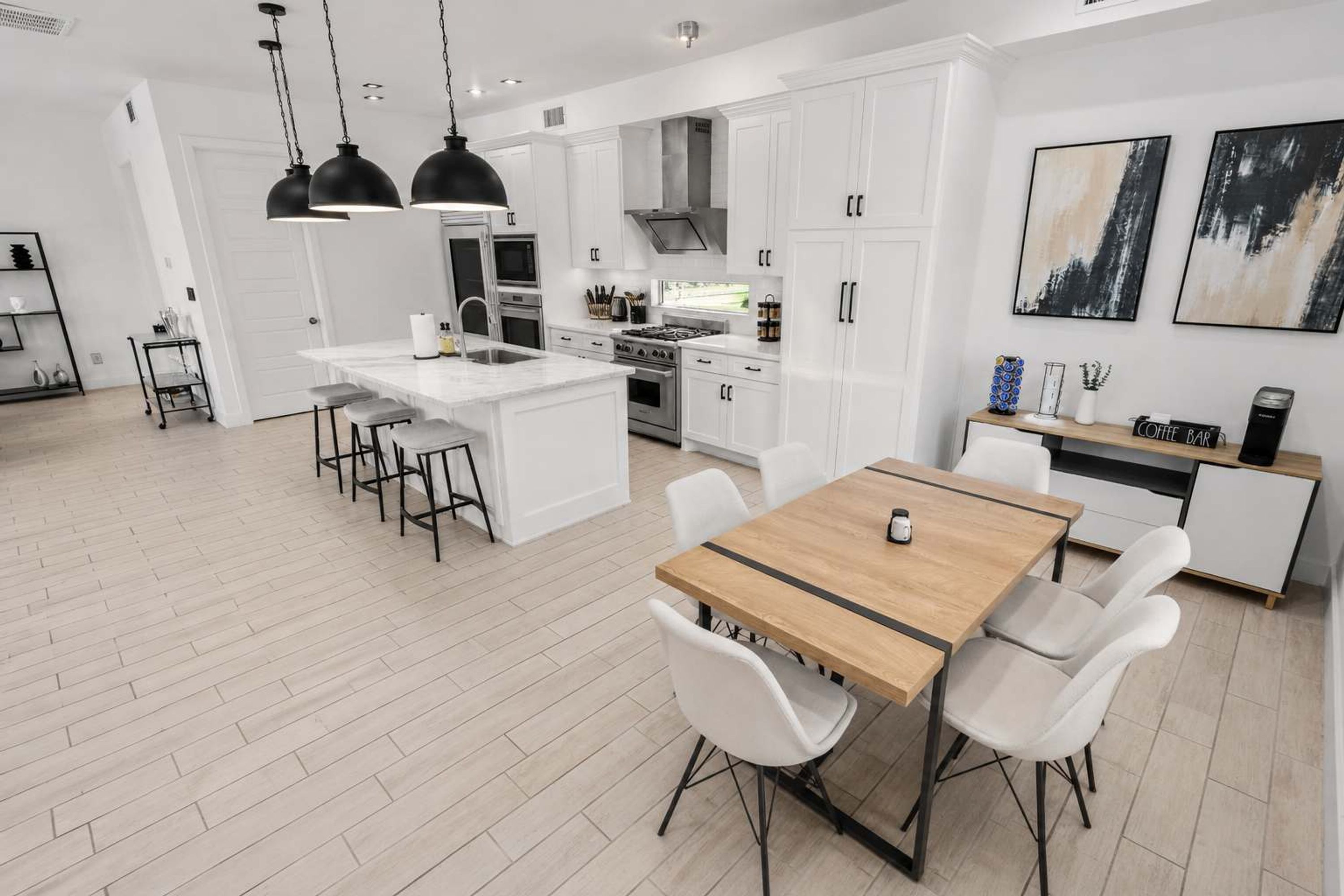 A modern kitchen with white cabinetry, a central island, and a dining area with a wooden table and white chairs.