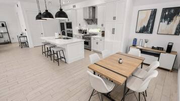 A modern kitchen with white cabinetry, a central island, and a dining area with a wooden table and white chairs.