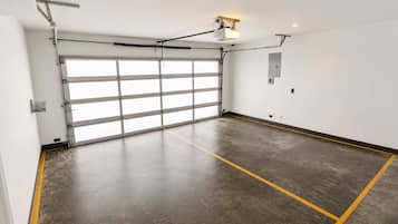 Un garaje limpio y vacío con una puerta grande, piso de concreto con líneas amarillas e iluminación colgante.