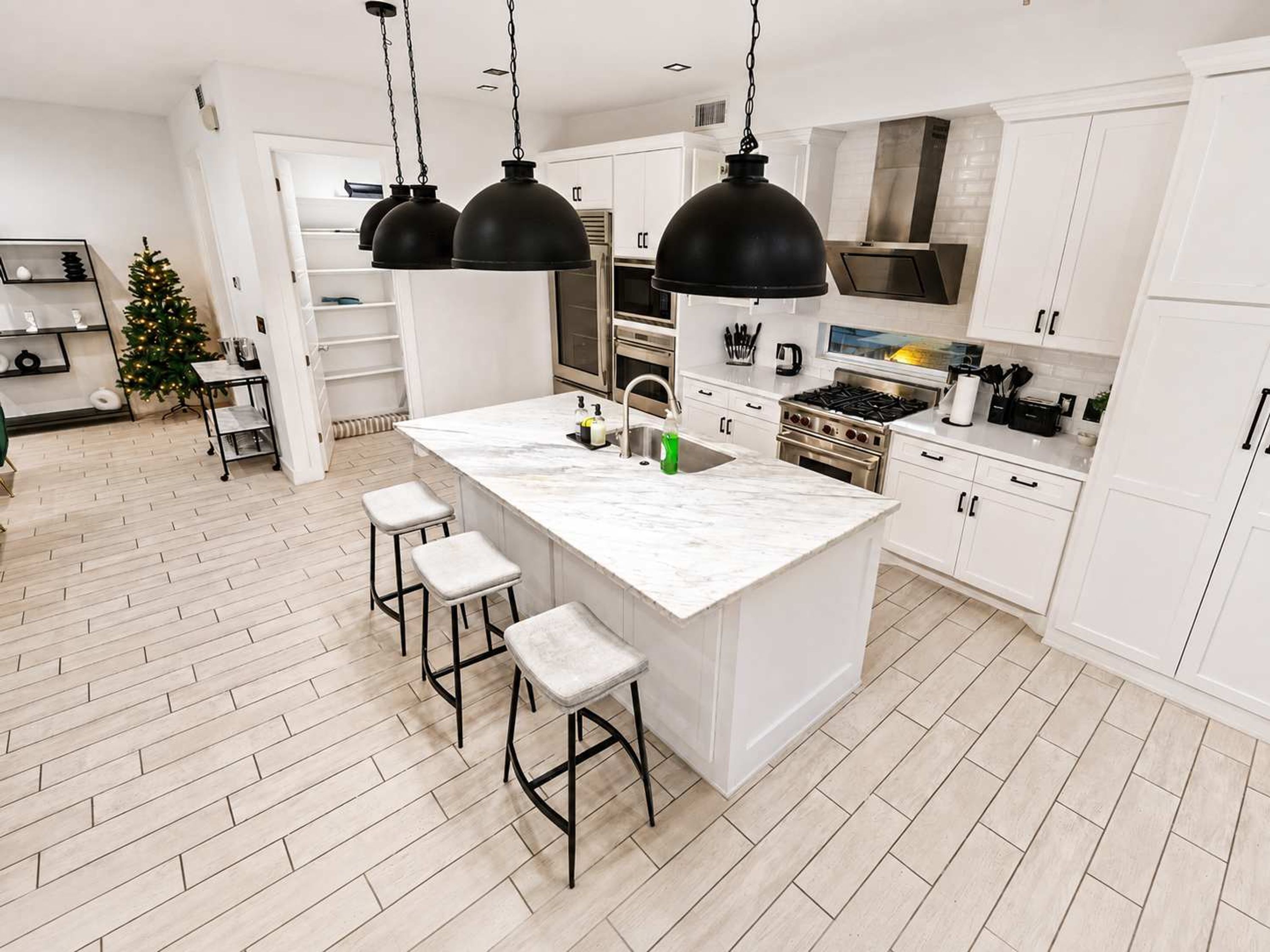 Une cuisine moderne avec des meubles blancs, un îlot en marbre et des suspensions noires.