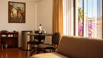 Habitación de hotel con sofá, mesa de comedor, sillas, un cuadro y vista a flores a través de la ventana.